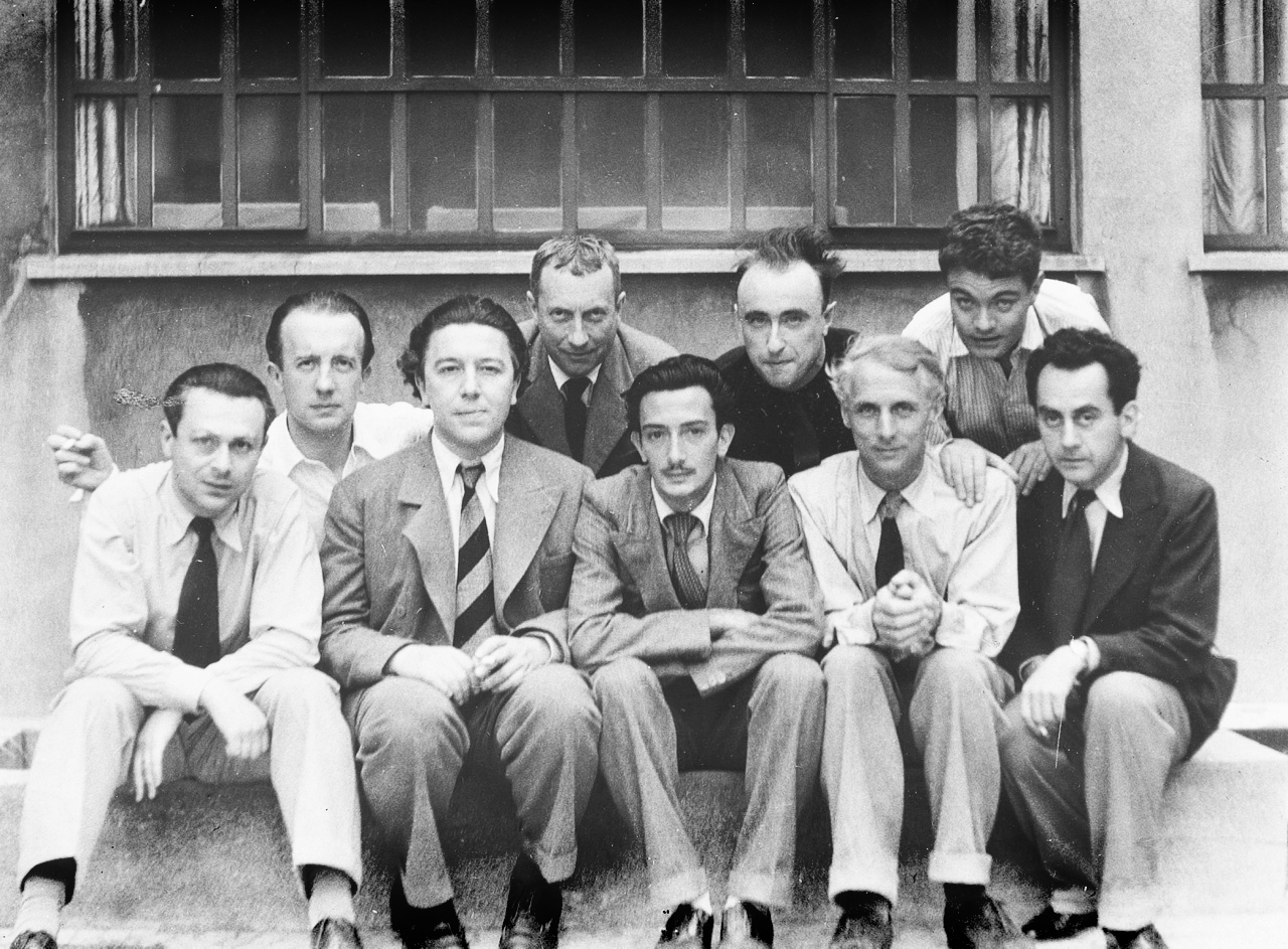 De izquierda a derecha: Tristan Tzara, Paul Eluard, André Breton, Hans Arp, Salvador Dalí, Yves Tanguy, Max Ernst, René Crevel, Man Ray.